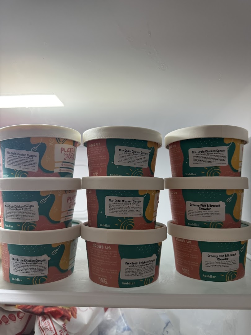 Containers of 'Plate & Play' toddler food, including congee and chowder, displayed in a fridge.