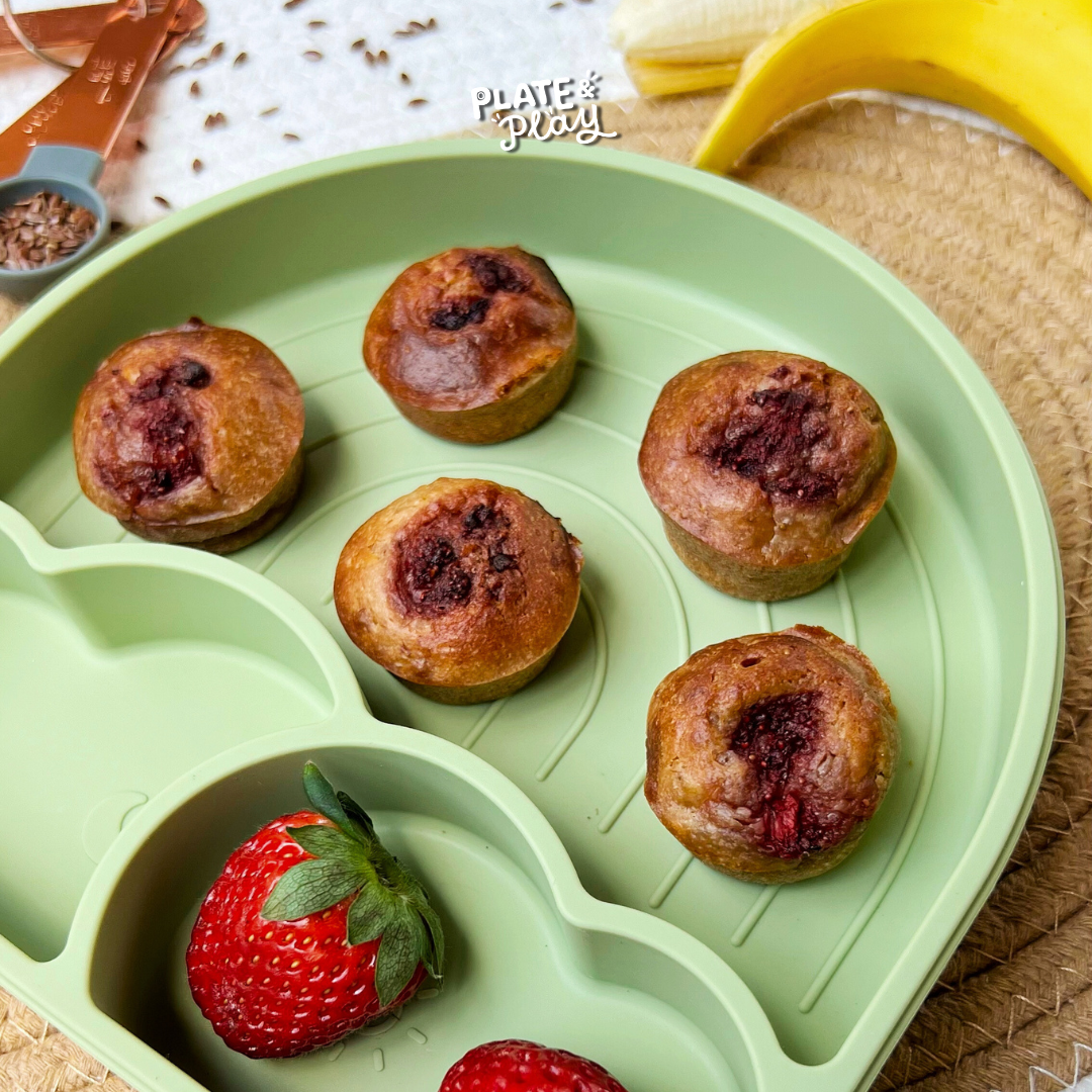 Mini fruit-filled muffins and fresh fruit on a green sectioned plate, showcasing healthy snacks.