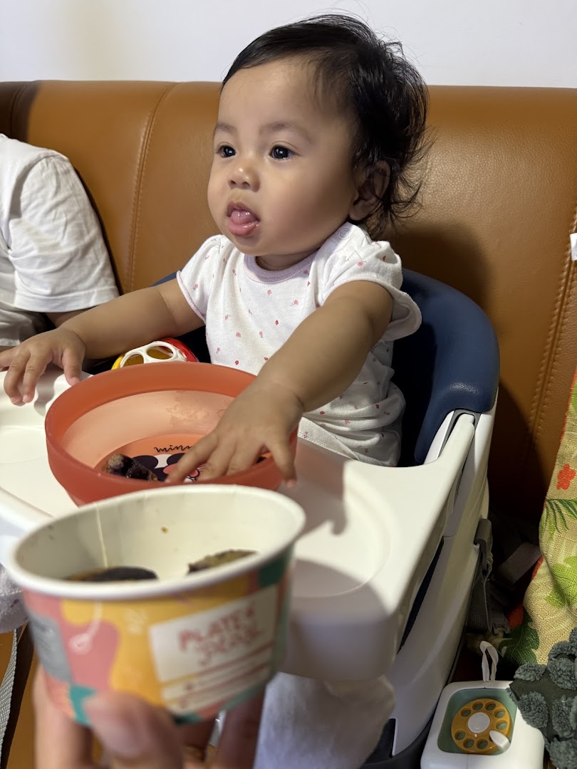 A baby in a high chair with a branded cup from Plate Play, enjoying a meal.