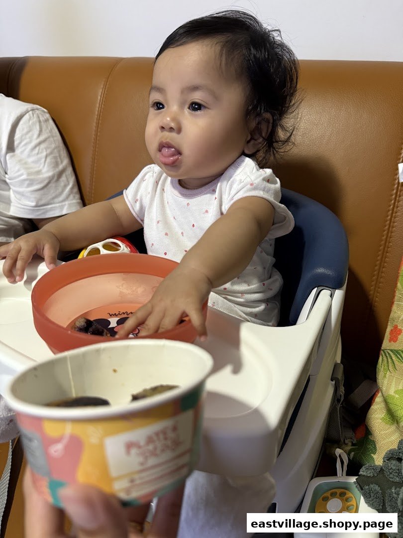 A baby in a high chair with a branded cup from Plate Play, enjoying a meal.