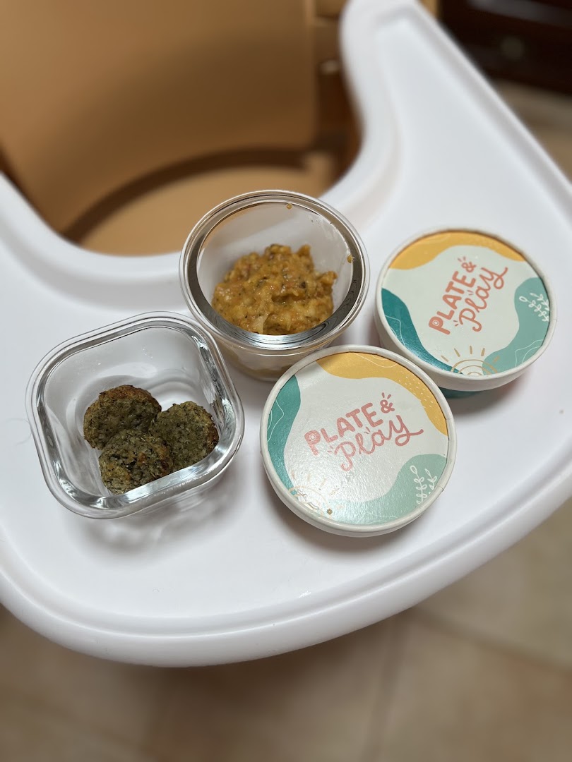 Portioned baby food from Plate & Play in containers on a high chair tray.