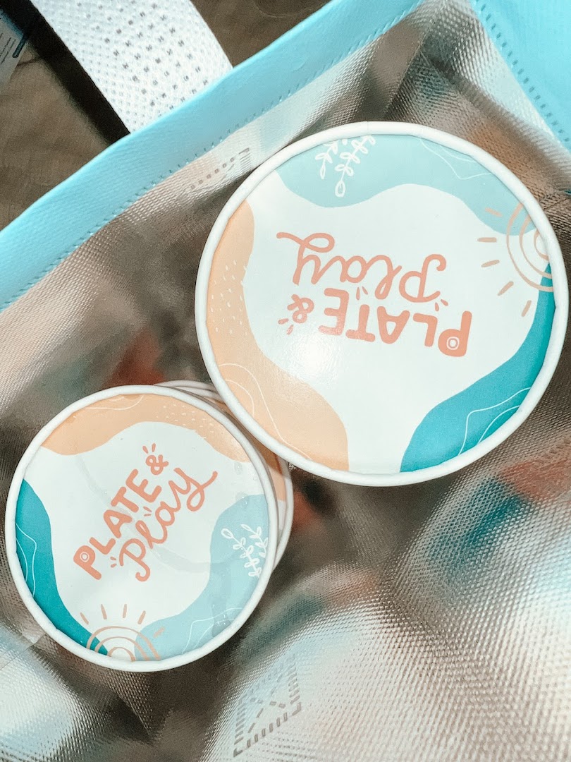 Close-up of colorful 'Plate & Play' branded coasters or lids inside a cooler bag.