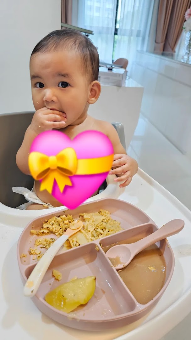 A baby in a high chair enjoys a meal from a divided plate.