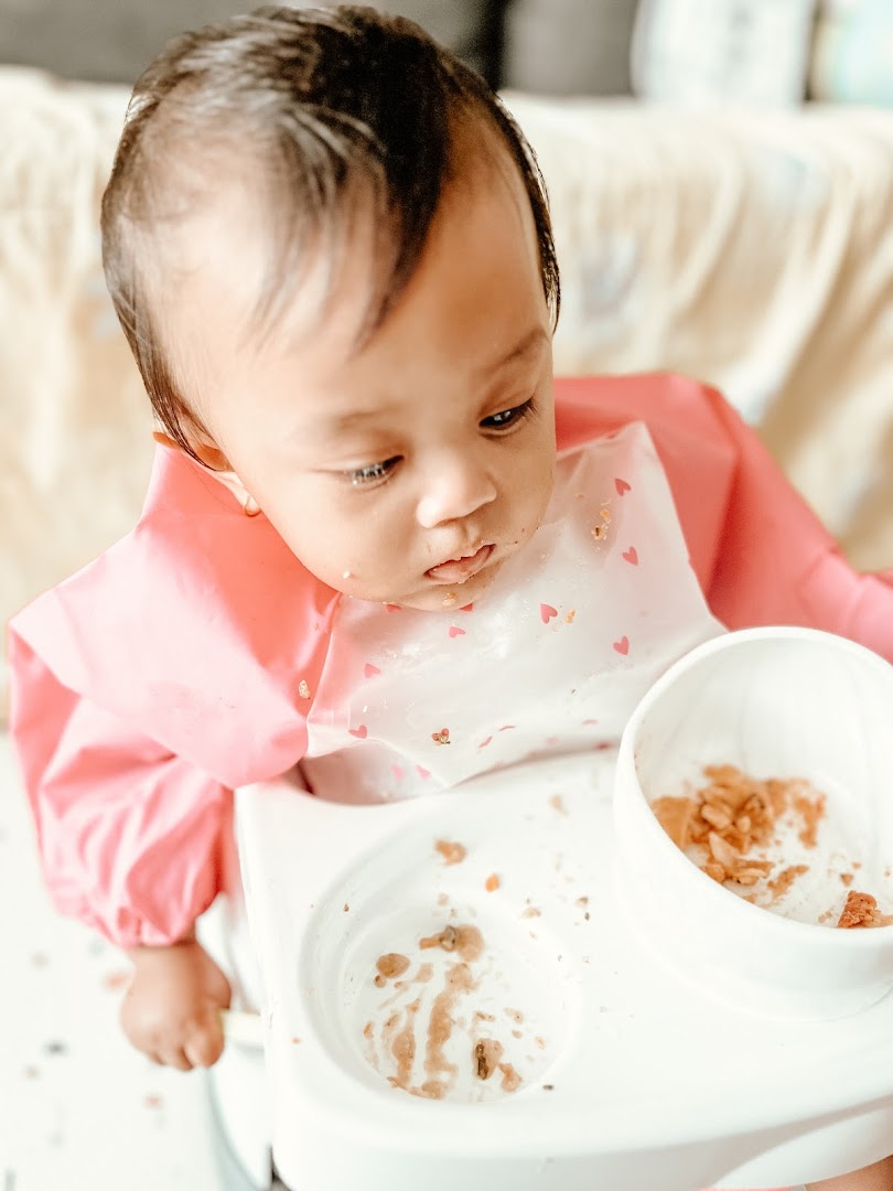 A baby in a high chair with a messy tray after eating, wearing a pink bib.