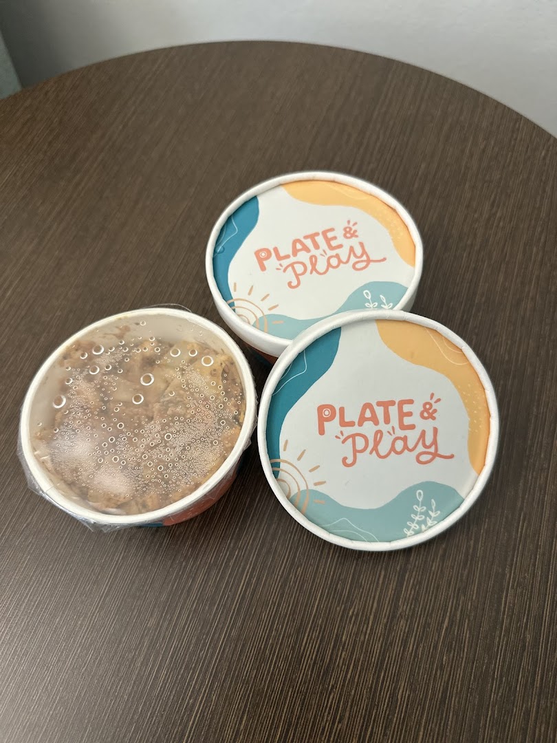 Three Plate & Play food containers, two with lids featuring the logo, one open with food.