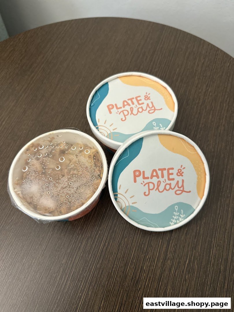 Three Plate & Play food containers, two with lids featuring the logo, one open with food.