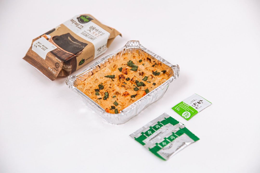 A baked rice dish in a foil container, accompanied by seasoned seaweed and condiment packets.