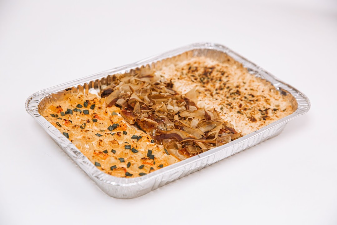 A rectangular foil tray filled with a baked dish featuring three distinct sections of toppings.