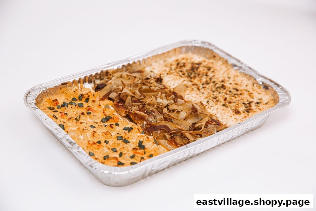 A rectangular foil tray filled with a baked dish featuring three distinct sections of toppings.