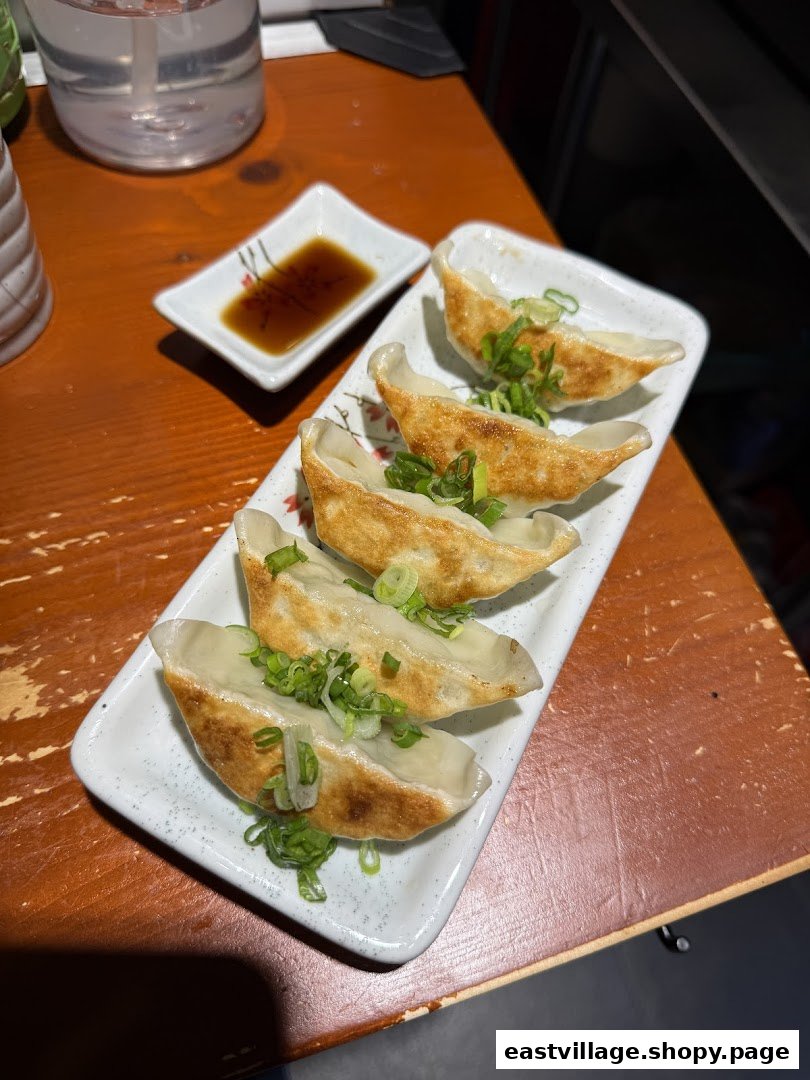 A plate of golden-brown gyoza topped with green onions, served with soy sauce on a wooden table.