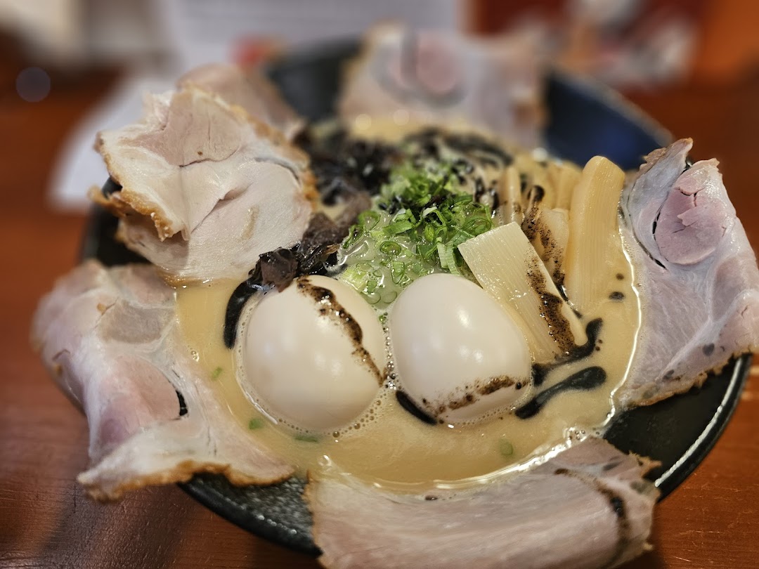 A close-up of a rich ramen bowl featuring tender pork slices, soft-boiled eggs, bamboo shoots, and green onions.