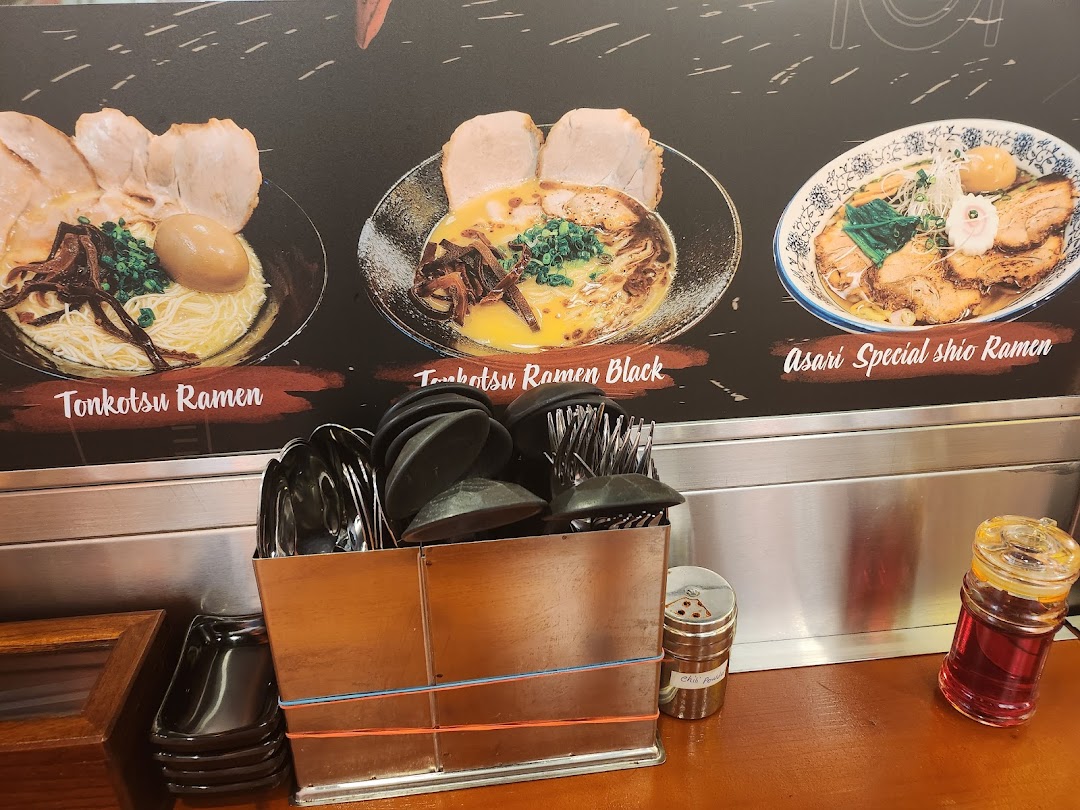 A visual menu board displaying three ramen dishes above a counter with utensils and condiments.
