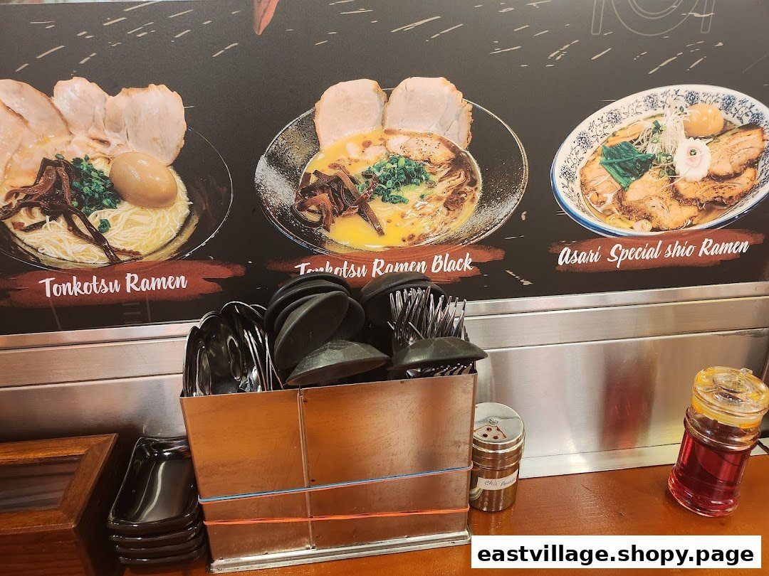 A visual menu board displaying three ramen dishes above a counter with utensils and condiments.