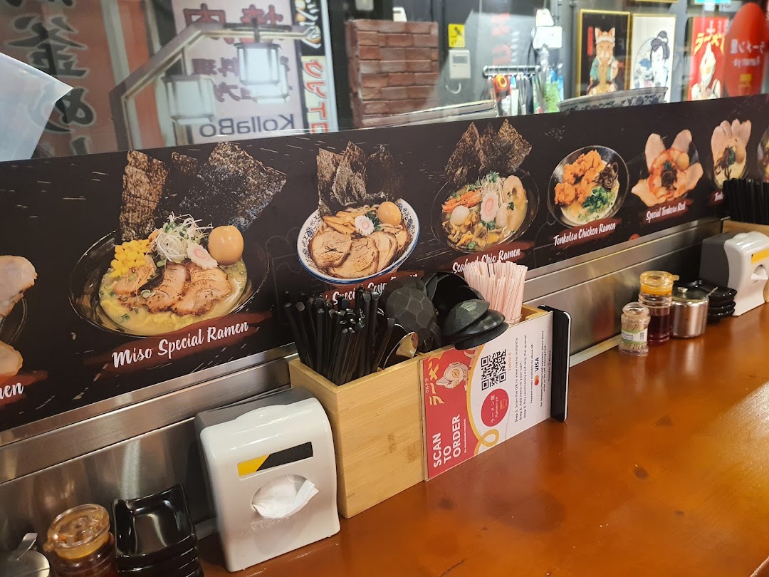 A ramen shop counter displaying various ramen dishes with names and a 'Scan to Order' QR code.