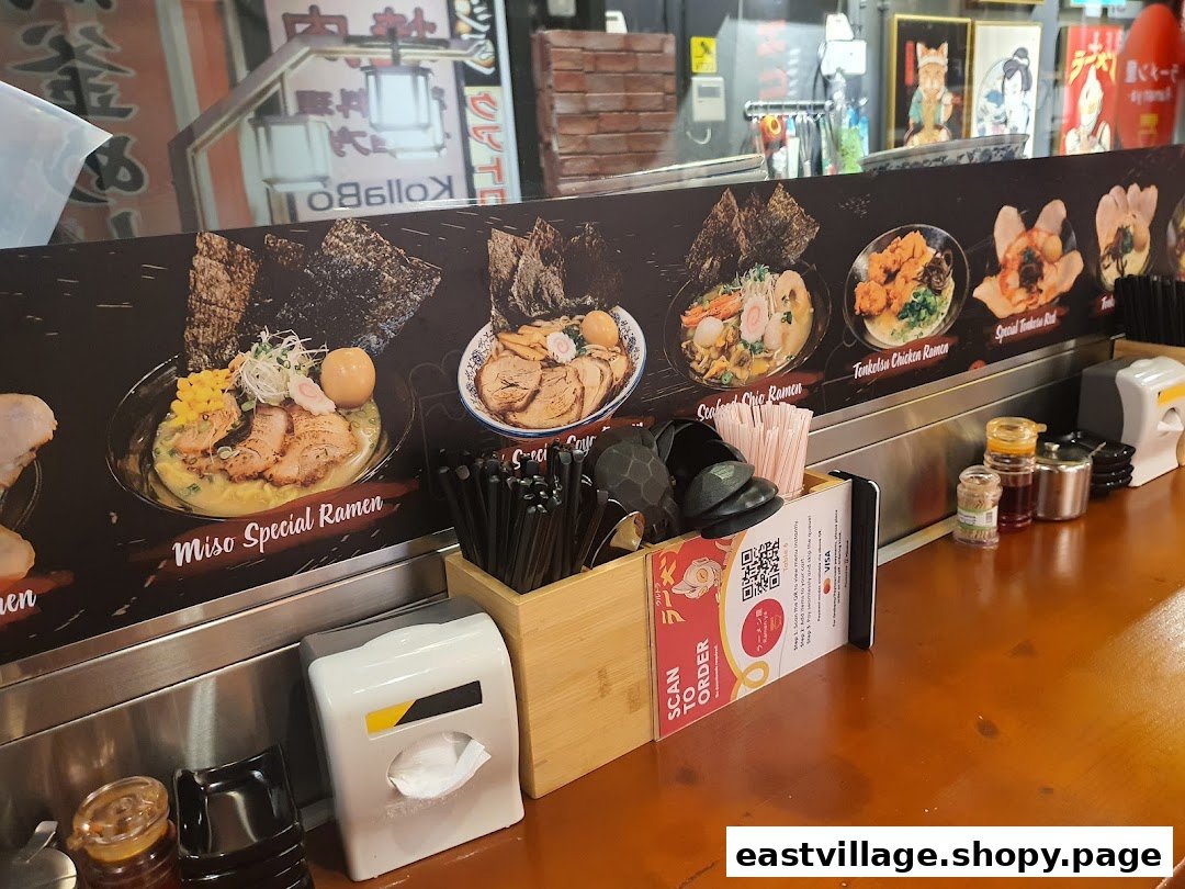 A ramen shop counter displaying various ramen dishes with names and a 'Scan to Order' QR code.