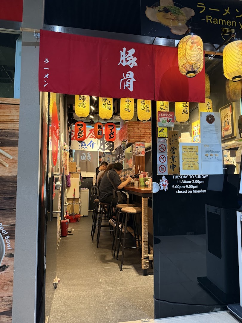 The entrance of Ramen-ya, a Japanese ramen shop, featuring a red banner, lanterns, and customers enjoying meals inside.
