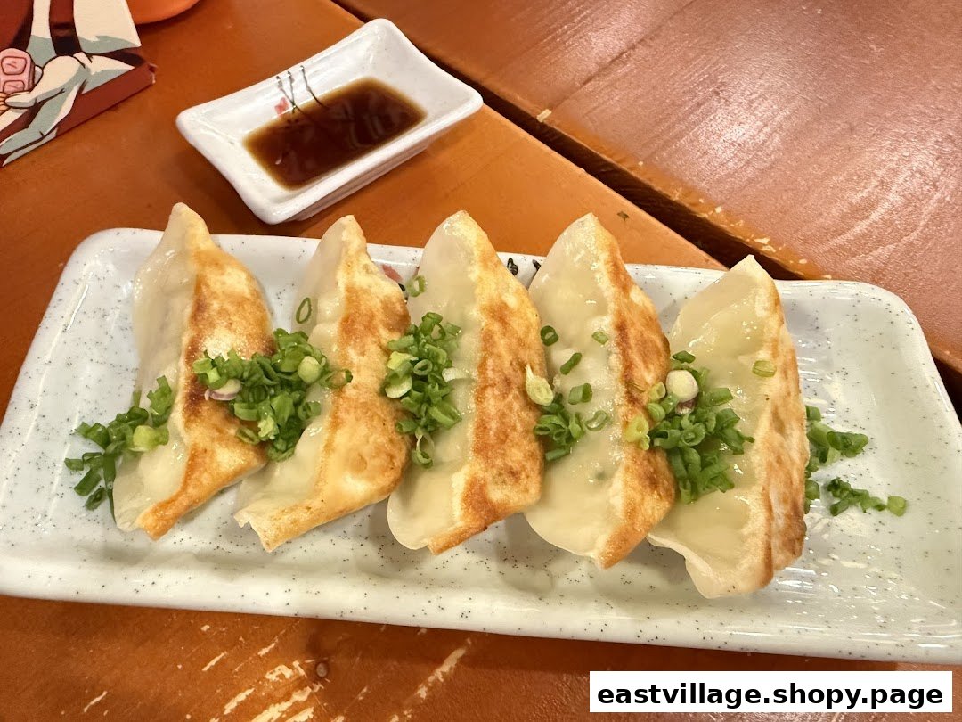 A plate of pan-fried gyoza with green onions and a side of dipping sauce.