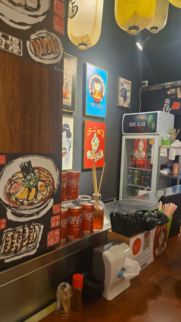Interior view of a vibrant ramen shop with Japanese-themed decor, counter seating, and a beverage fridge.