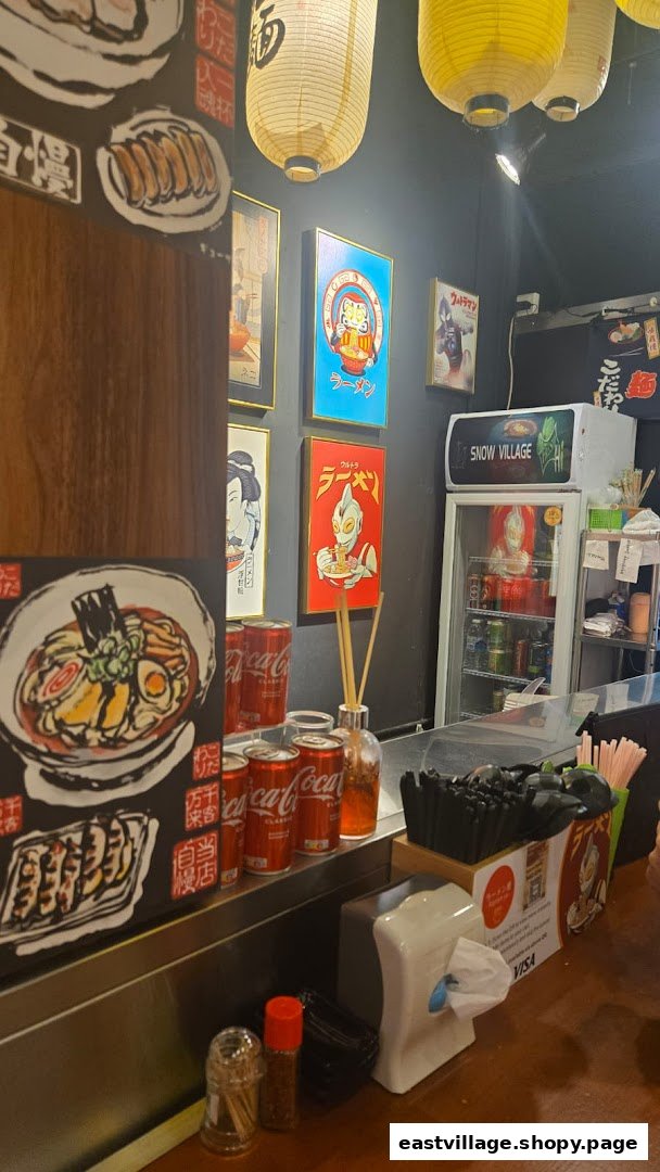 Interior view of a vibrant ramen shop with Japanese-themed decor, counter seating, and a beverage fridge.