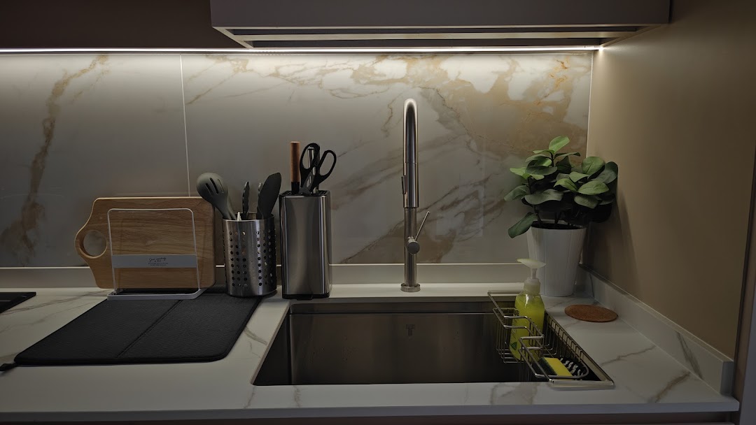 A modern kitchen sink area with marble backsplash, kitchen tools, and a decorative plant.