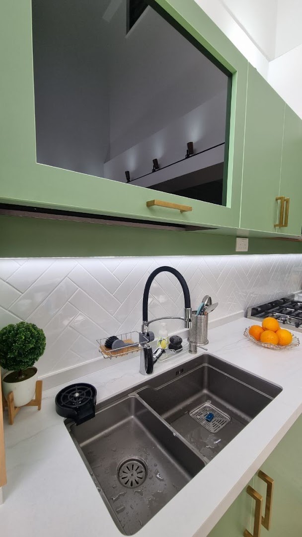 A modern kitchen interior featuring a double sink, light green cabinets, and white herringbone backsplash.