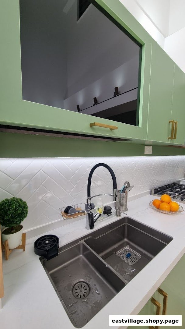 A modern kitchen interior featuring a double sink, light green cabinets, and white herringbone backsplash.