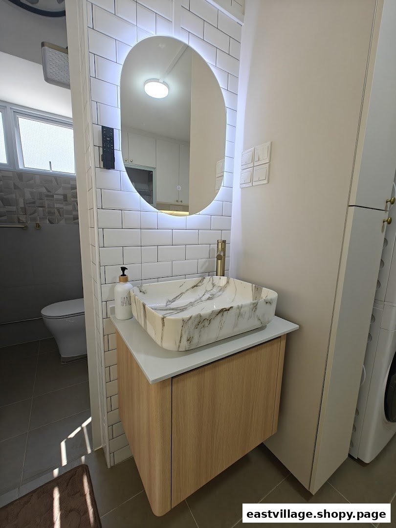 A modern bathroom features a stylish marble-patterned vessel sink, a wooden vanity, and an illuminated oval mirror.