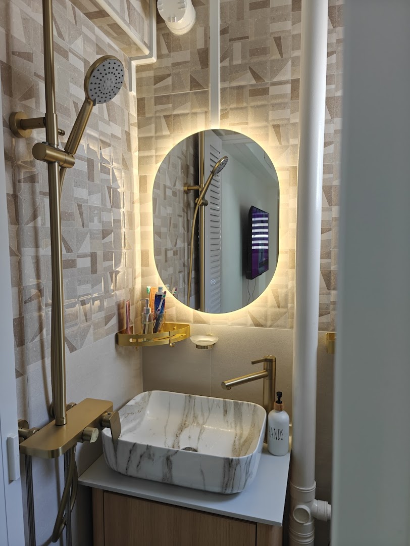 A modern bathroom interior featuring a marble vessel sink, gold fixtures, and an illuminated mirror.