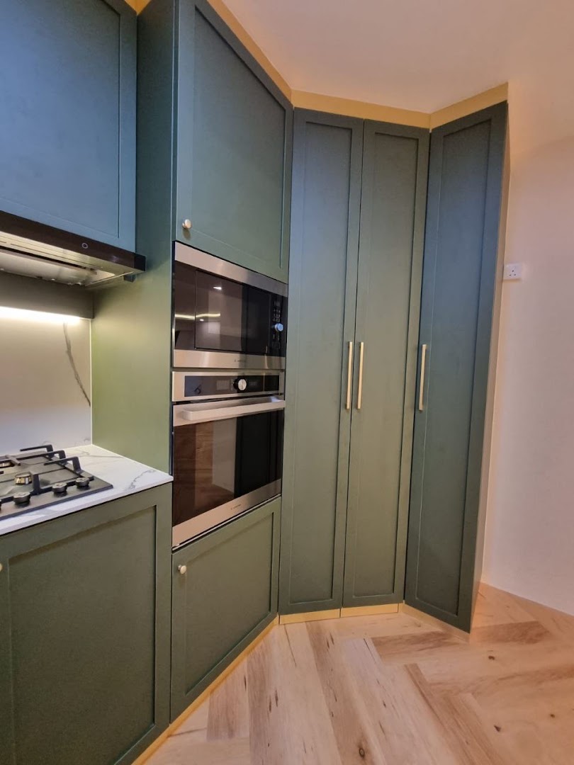 A modern kitchen featuring dark green cabinetry, integrated appliances, and light wooden herringbone flooring.