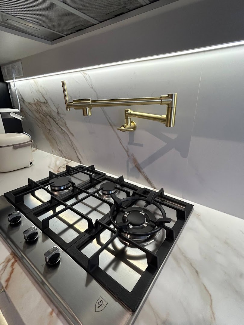 A modern kitchen featuring a sleek gas hob, marble backsplash, and a stylish gold pot filler faucet.