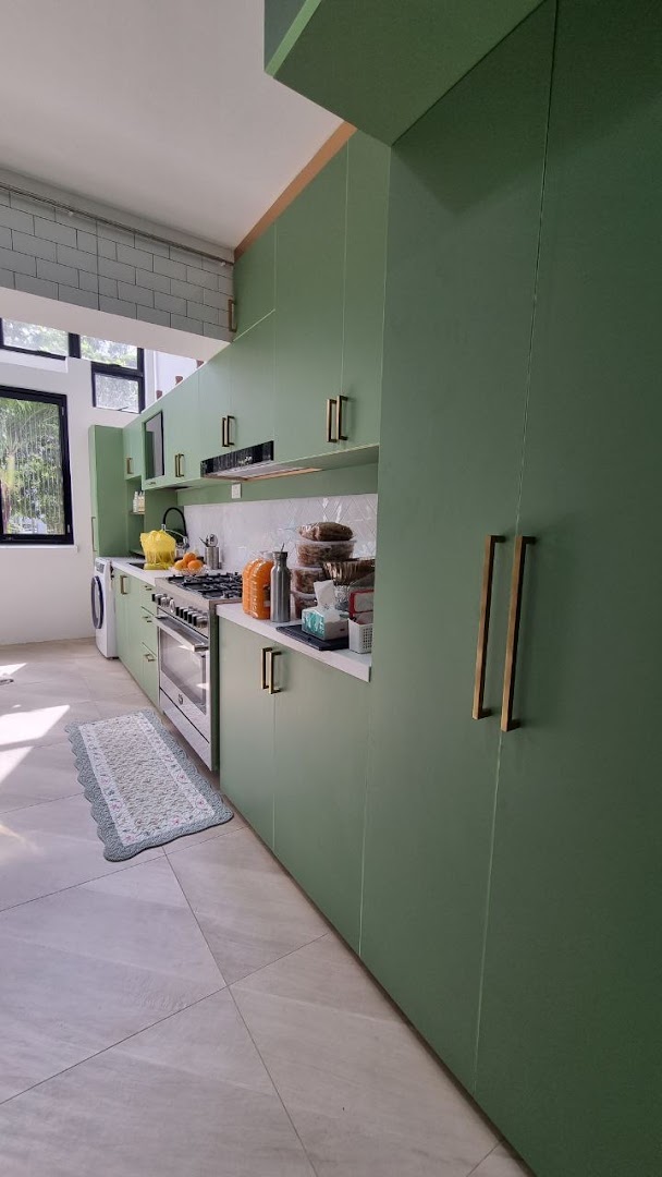 A modern kitchen interior featuring sage green cabinets, white countertops, and stainless steel appliances.