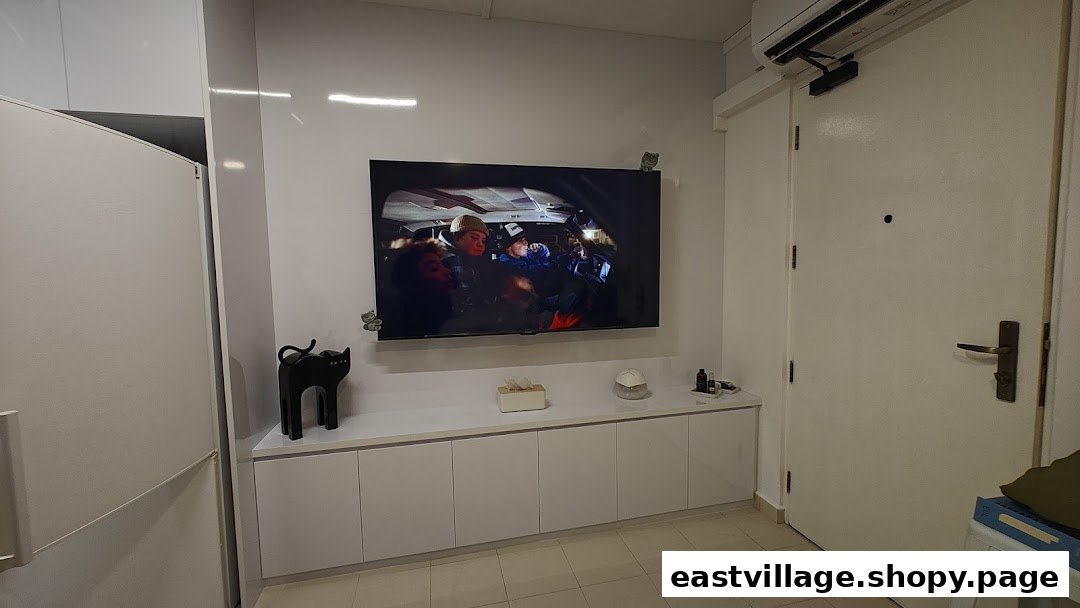 A modern, minimalist interior featuring a wall-mounted TV, sleek white cabinets, and a clean aesthetic.