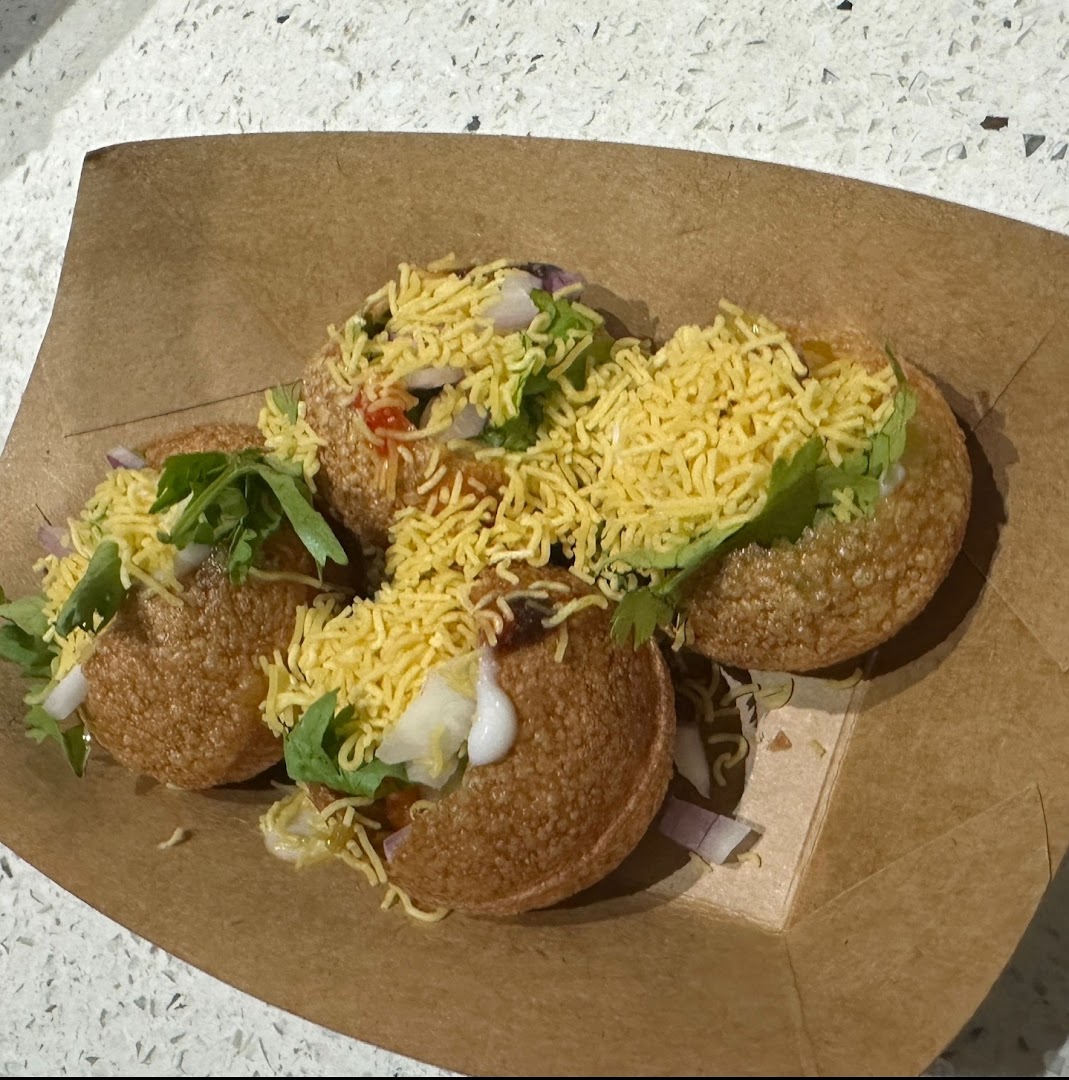 Close-up of delicious Indian street food, likely pani puri, served in a brown paper tray.