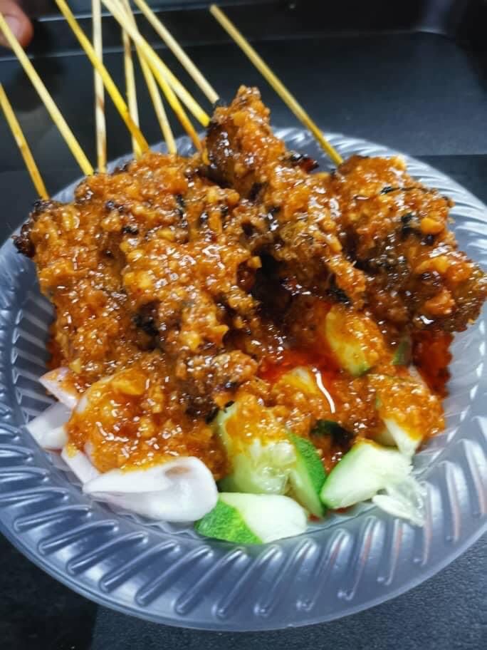 Close-up of delicious satay skewers generously coated in peanut sauce, served with cucumber and onion.