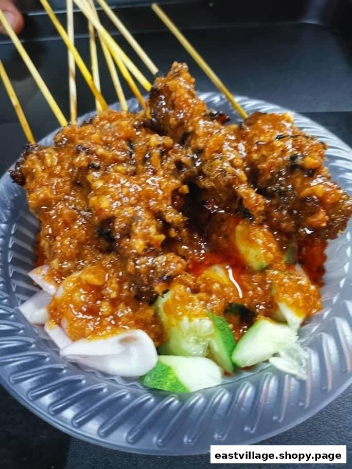 Close-up of delicious satay skewers generously coated in peanut sauce, served with cucumber and onion.