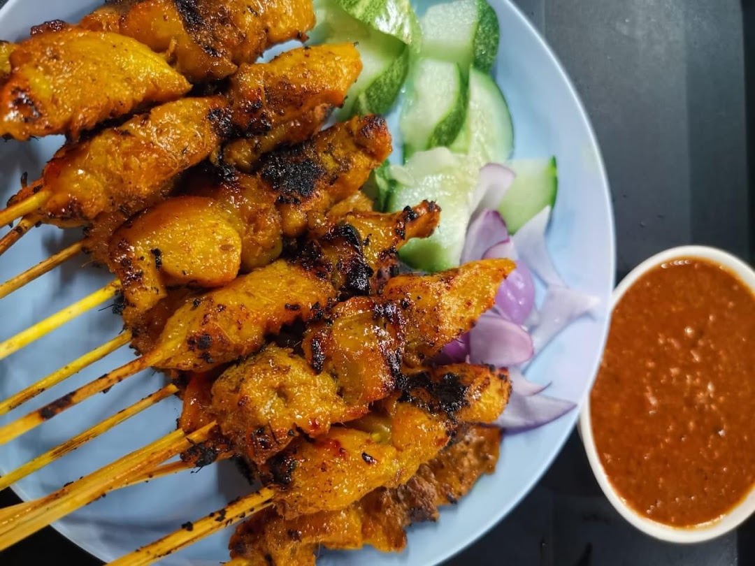 A plate of grilled satay skewers with peanut sauce, cucumber, and red onion.
