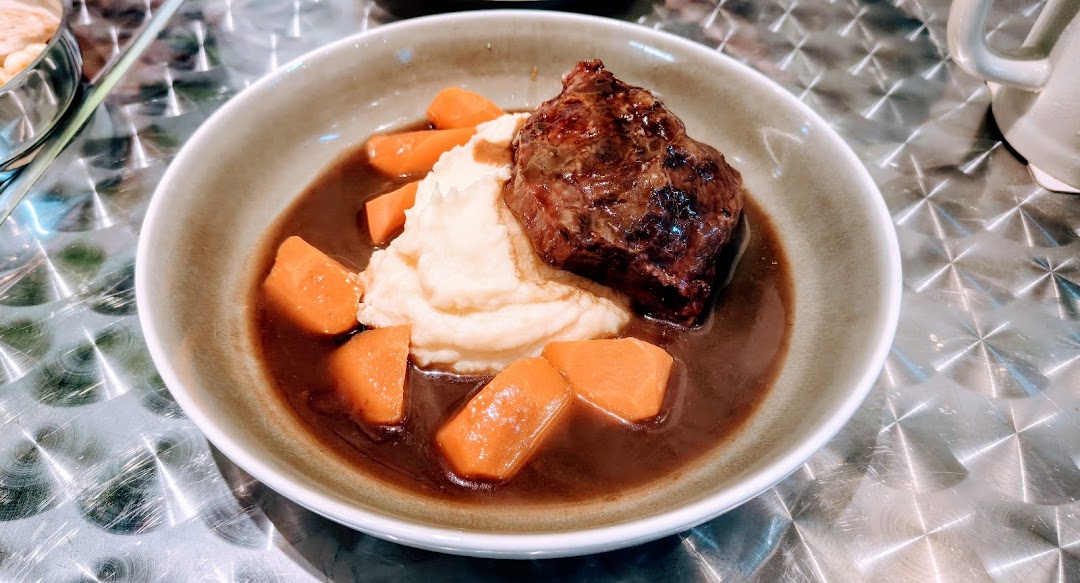 A hearty dish featuring braised meat, creamy mashed potatoes, and carrots in rich gravy.