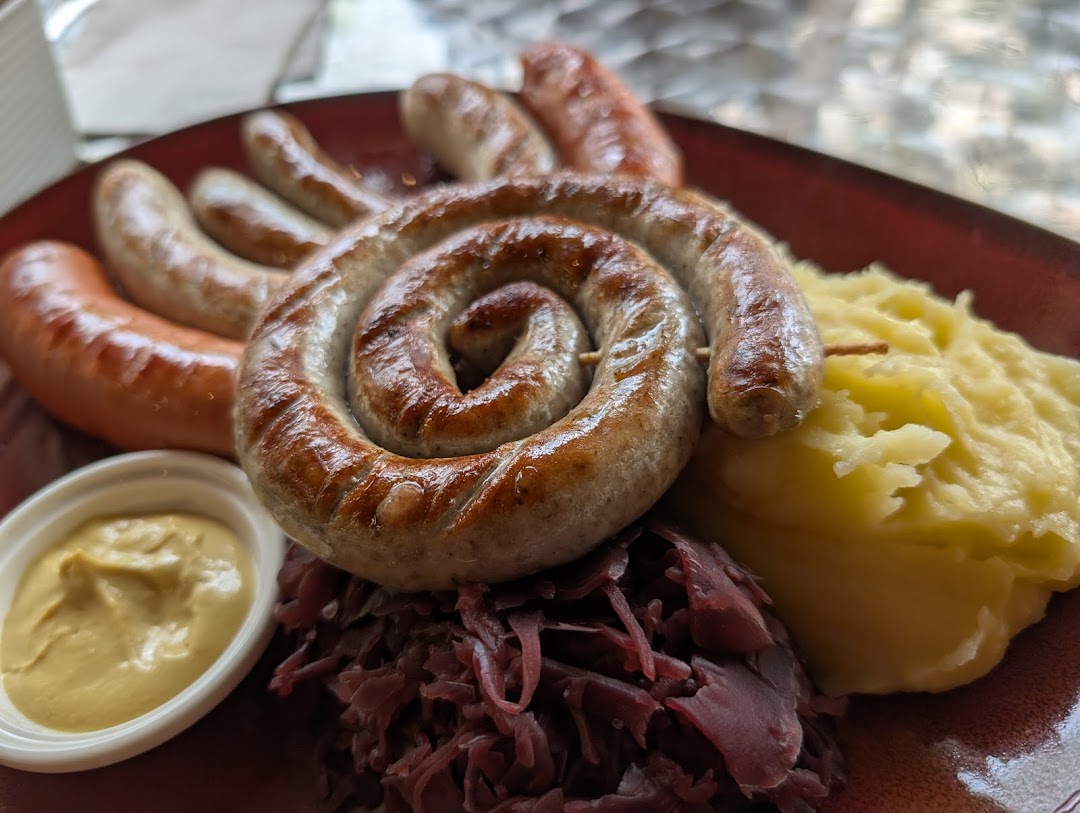 A plate of grilled sausages, including a coiled one, served with mashed potatoes, red cabbage, and mustard.