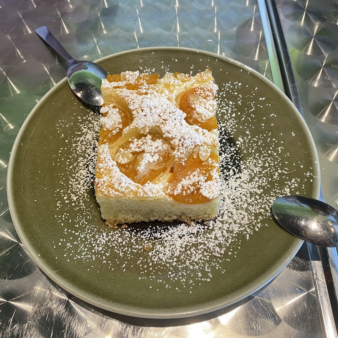 A delicious slice of apricot cake, dusted with powdered sugar, served on a green plate.