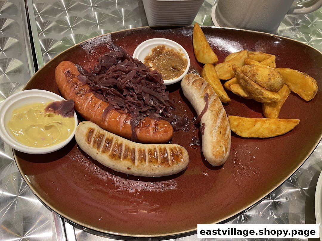 A hearty plate featuring two grilled sausages, red cabbage, potato wedges, and dipping sauces.