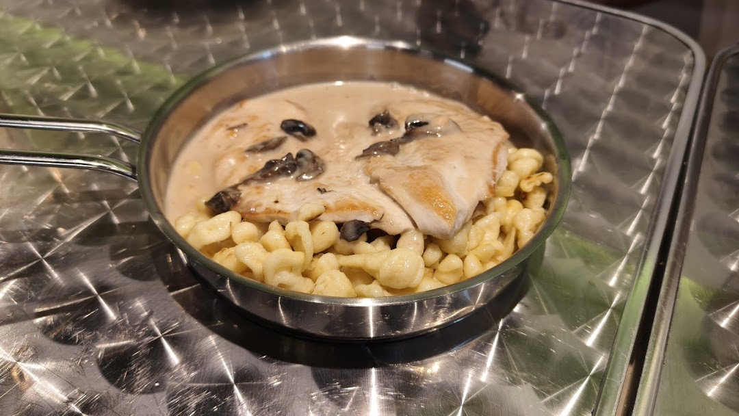 A hearty dish featuring chicken in creamy mushroom sauce with spaetzle, served in a metal pan.