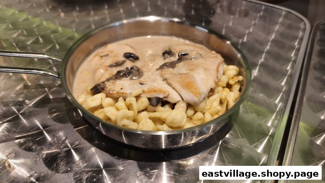 A hearty dish featuring chicken in creamy mushroom sauce with spaetzle, served in a metal pan.