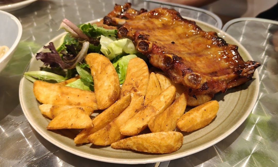 A delicious plate of glazed ribs served with crispy potato wedges and a fresh side salad.