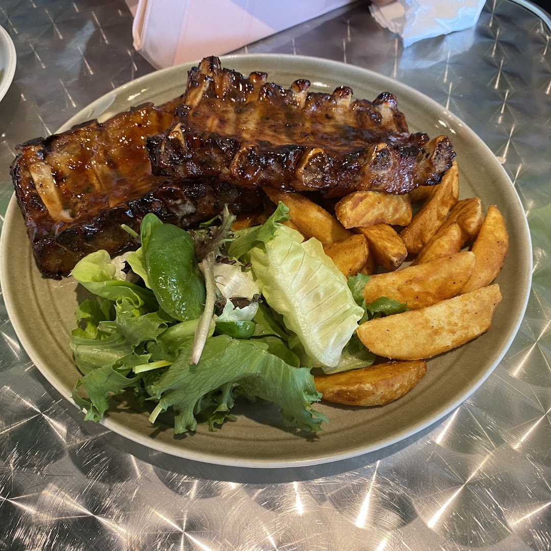 A plate of glazed ribs served with crispy potato wedges and a fresh green salad.