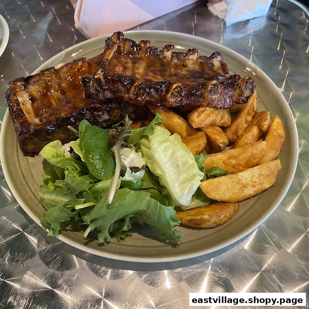 A plate of glazed ribs served with crispy potato wedges and a fresh green salad.