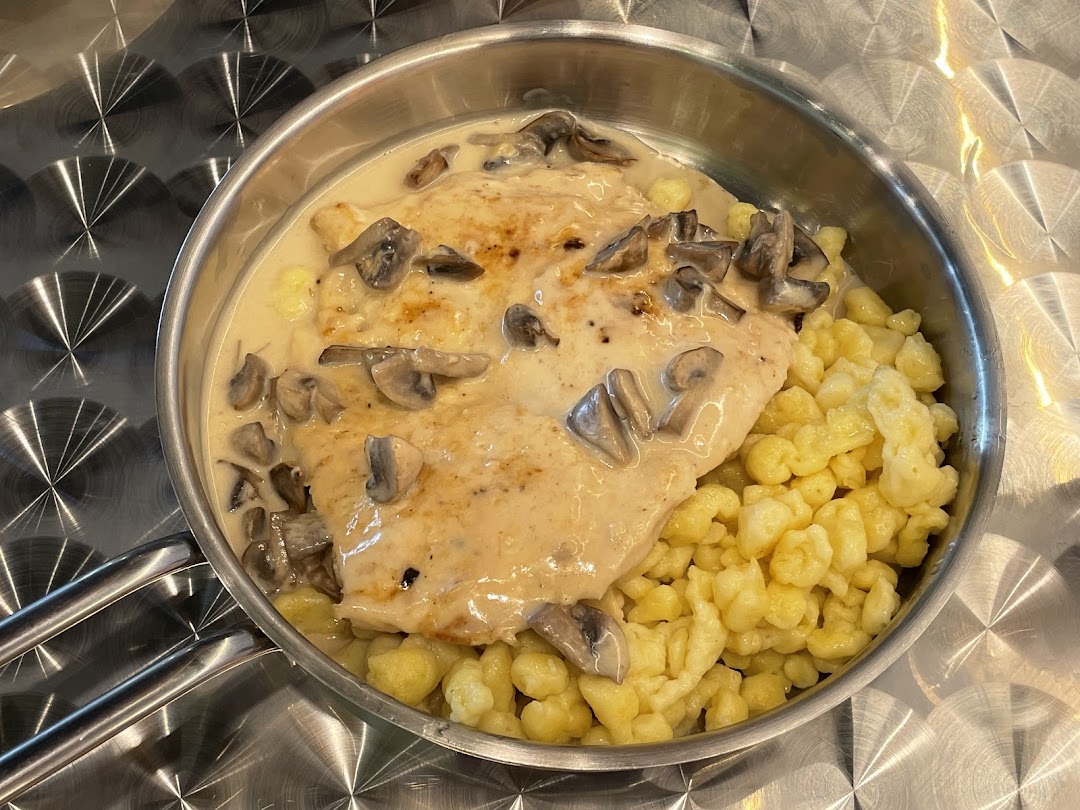 A delicious schnitzel with creamy mushroom sauce and spaetzle served in a metal pan.