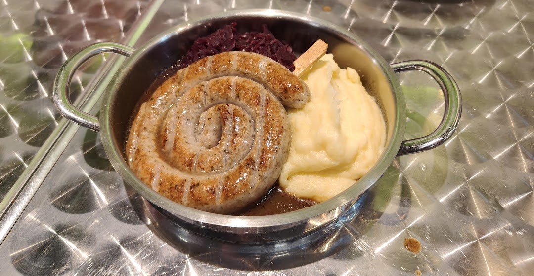 A hearty dish featuring a coiled sausage, mashed potatoes, and red cabbage served in a small pot.