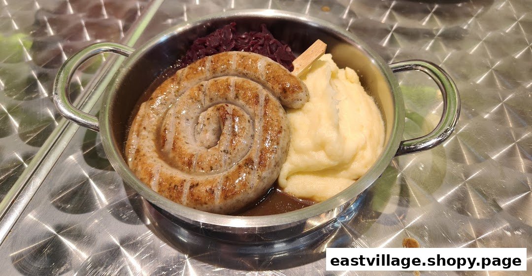 A hearty dish featuring a coiled sausage, mashed potatoes, and red cabbage served in a small pot.