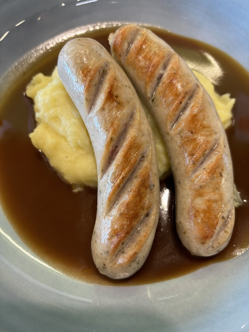 Two grilled sausages served with creamy mashed potatoes and rich gravy in a bowl.