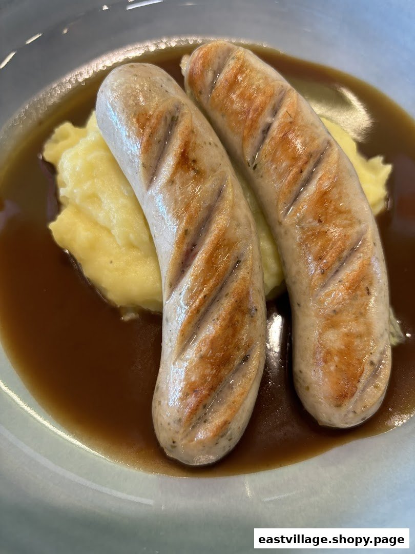 Two grilled sausages served with creamy mashed potatoes and rich gravy in a bowl.